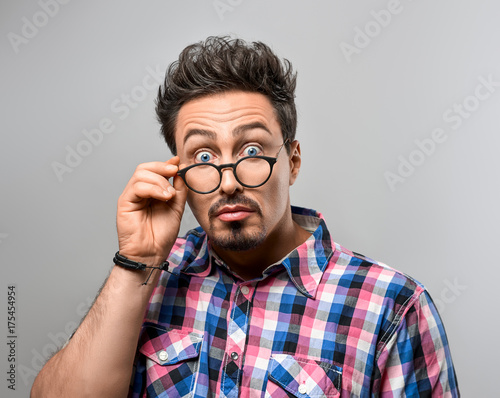 Handsome young man Having Fun Crazy. Surprised Gesturing. Portrait Hipster Nerd guy in Trendy shirt, Glasses. Brunette Bearded Emotional Stylish Hairstyle on gray background. Blue Eyes