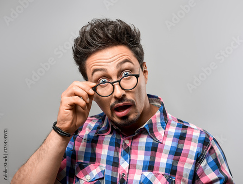 Handsome young man Having Fun Crazy. Surprised Gesturing, Open Mouth. Portrait Hipster Nerd guy in Trendy shirt, Glasses. Brunette Bearded Emotional Stylish Hairstyle on gray background. Blue Eyes