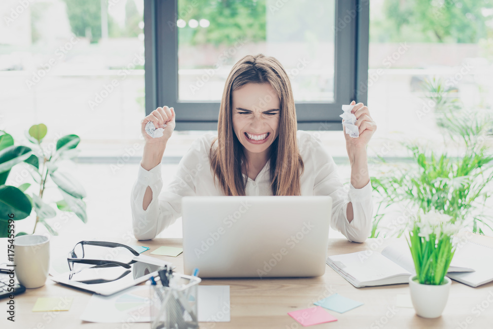 Intelligent brown haired business lady faced a challenge and cramps the documents. She got bad news on internet, going crazy while sitting at her work place, gesturing with fists, windows behind her Intelligent brown haired business lady faced a challenge and cramps the documents. She got bad news on internet, going crazy while sitting at her work place, gesturing with fists, windows behind her