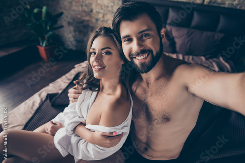 Fotografie Close up photo of beautiful half naked brunet young couple embracing, sitting in bedroom, guy takes selfie, so tender, romantic, tempting, sensual