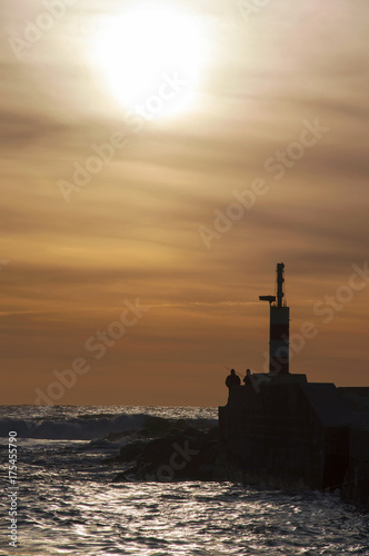 Small lighthouse and fishermen by the beach shore, during sunset © Rafael