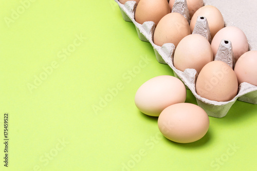 Chicken eggs in a cardboard box on a green background. Copy space for text