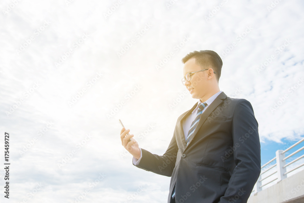 Young asian businessman wearing black suit smiling while using mobile phone Young asian businessman wearing black suit smiling while using mobile phone