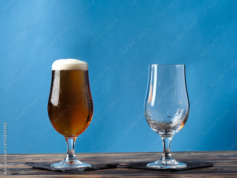 Empty glass and a glass of light beer on a blue background. Empty glass and a glass of light beer on a blue background.