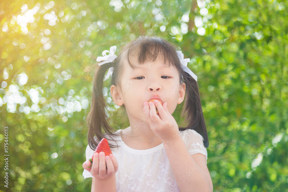 Little asian girl eating strawberry between picnic in park Little asian girl eating strawberry between picnic in park