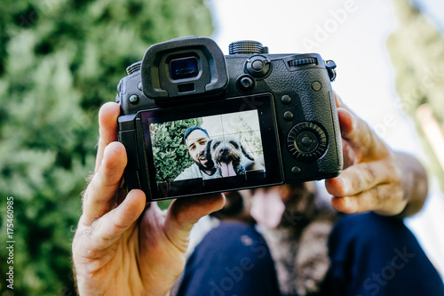 .Young man enjoying a sunny day in the park with his brown dog. They are taking a picture together with the camera. Lifestyle