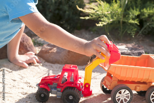 A child plays in the sand with big toy cars, an excavator, a truck