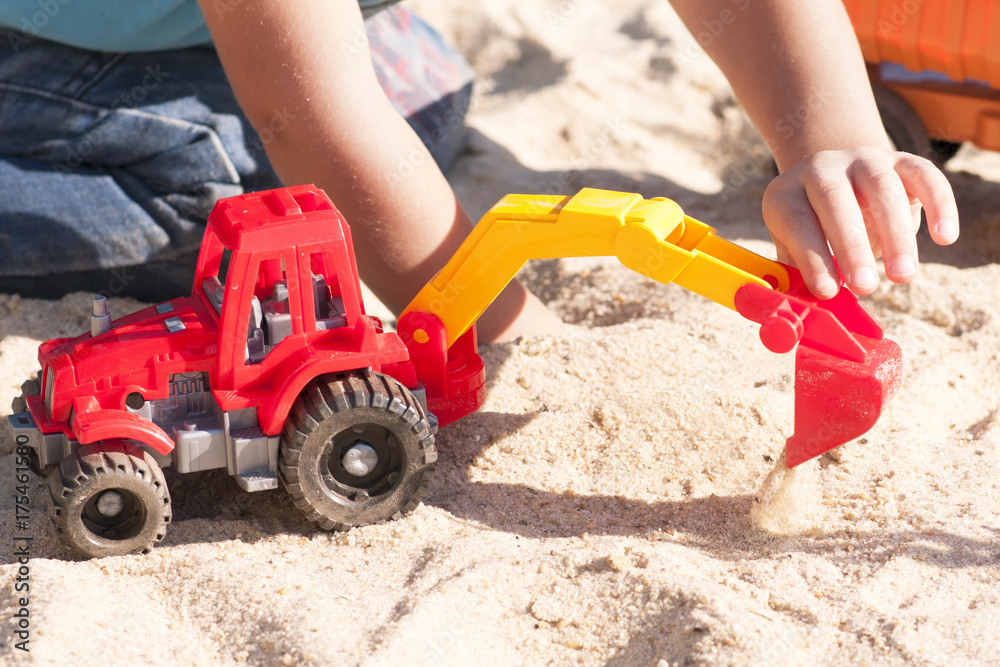 A child plays in the sand with big toy cars, an excavator, a truck A child plays in the sand with big toy cars, an excavator, a truck