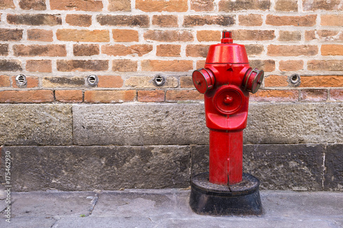 Red fire hydrant on the street on the brick wall background