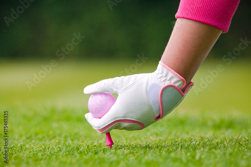 Lady golfer placing pink ball and tee into the ground.