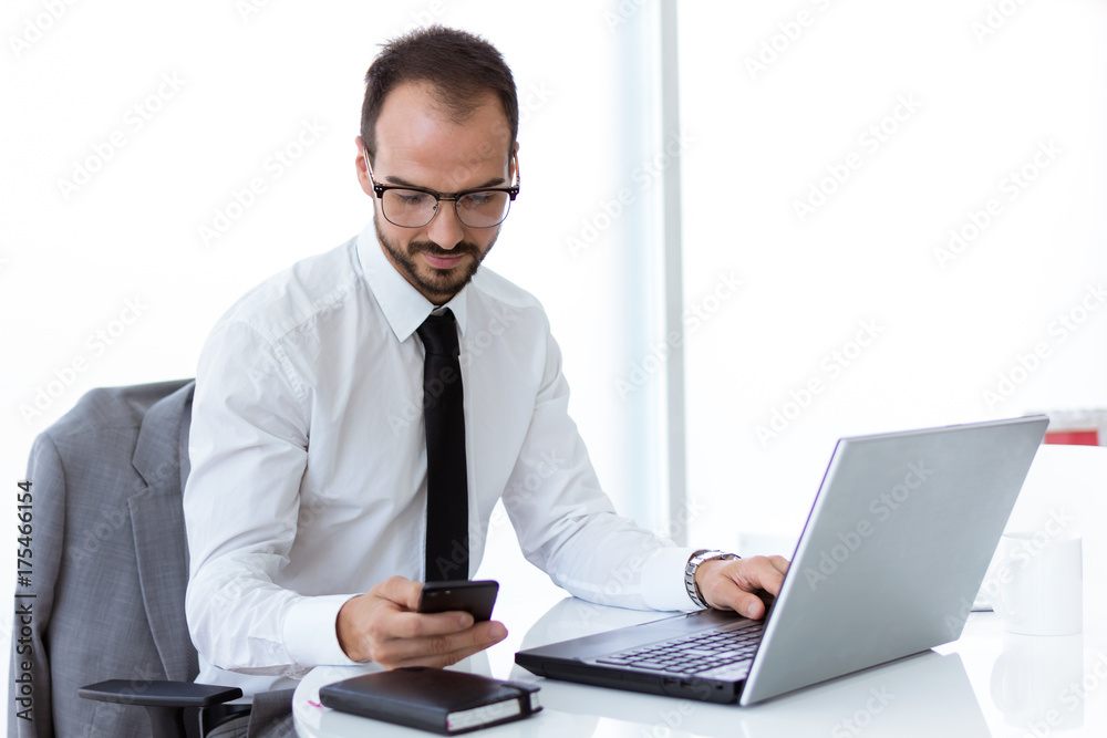 Handsome young man working with laptop and mobile phone in the office. Handsome young man working with laptop and mobile phone in the office.