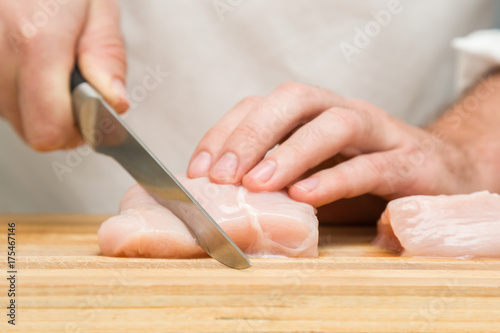 Chef's hands with a knife cutting a chicken meat on the wooden board in the kitchen. Preparation for cooking and baking. Food concept.