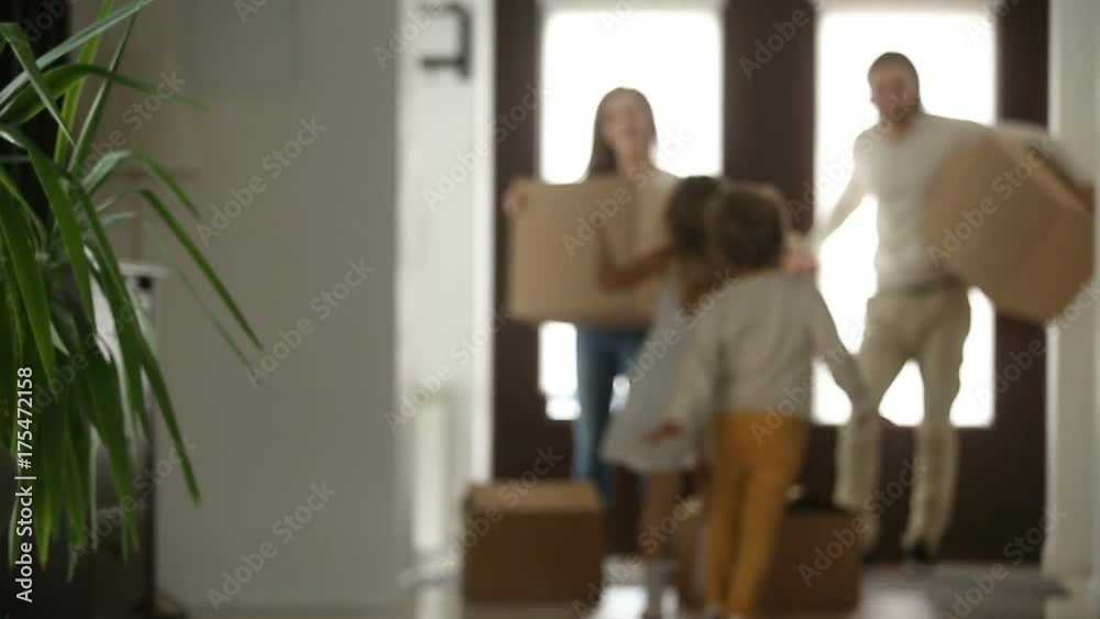 Excited kids boy and girl running into new home with parents holding boxes at background, happy couple with children and packed cardboards just moved in big modern house, family relocating concept