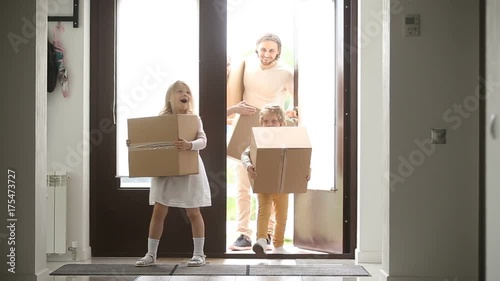 Happy family with kids holding boxes entering new modern house, excited couple and children relocating carrying belongings, opening entrance door looking around while moving in own bought rented home photo