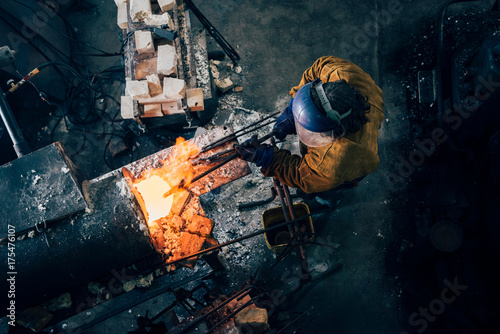 Overhead view of blacksmith shaping red hot metal rod in workshop furnace