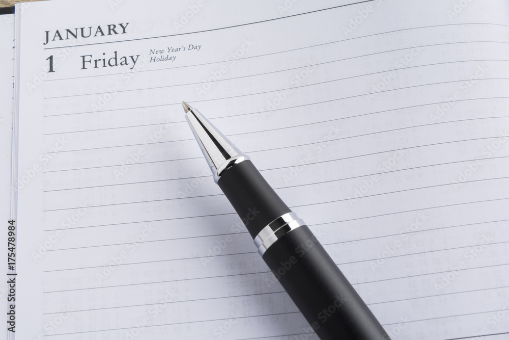 Metal pen on a calendar with the page showing the first day of the year in a setting goals concept Metal pen on a calendar with the page showing the first day of the year in a setting goals concept