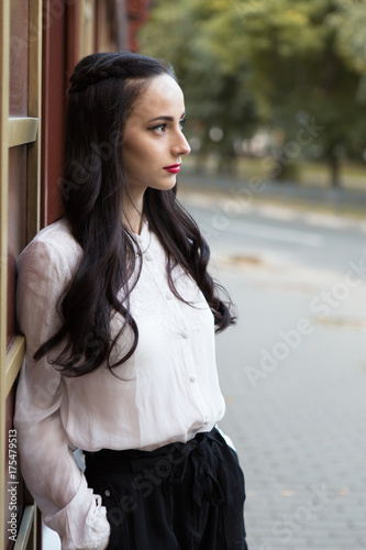 Portrait of young brunette woman in white blouse on the street