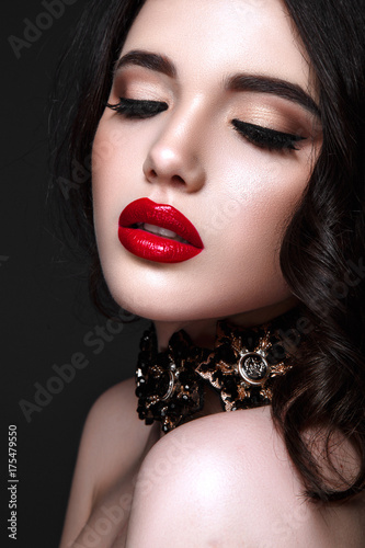 Beautiful woman portrait. Young lady posing close up on black background. Glamour make up, red lipstick. Gorgeous jewelry on neck.