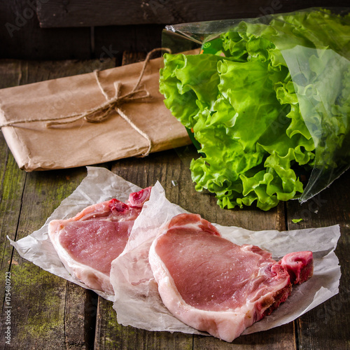 raw and fresh pork steak and lettuce leaves on a wooden surface