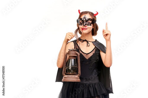 Portrait of beautiful she-devil posing with lantern on Halloween against white background photo