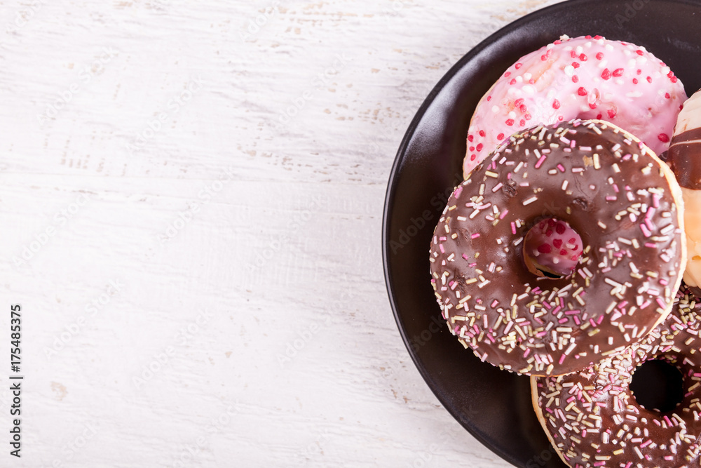 Delicious donuts in a black plate over white wooden background Delicious donuts in a black plate over white wooden background