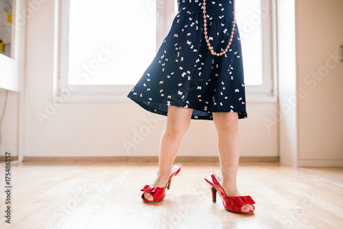 Unrecognizable little girl in dress and red high heels at home.