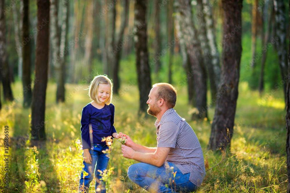 dad walks in the park with his beloved daughter at sunset, holds his hand and gives a bouquet of wild flowers