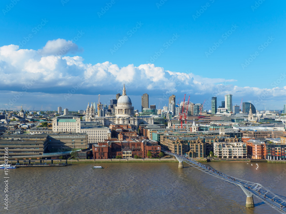 London skyline with a view of St Paul's Cathedral, Millennium Bridge and skyscrapers of the north bank of the River Thames on a sunny day.