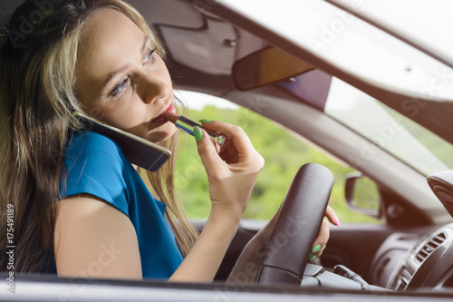 frivolous woman driving the car, painting her lips and talking on the phone