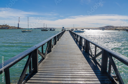 Wooden pier leading out into bay on sunny day with many boats  Luderitz  Namibia  Southern Africa