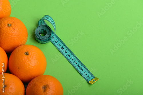 Oranges near long measuring tape on green background, top view