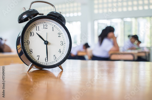 Closeup of Retro alarm clock with ten o'clock on table teacher in blur students exams classroom. Time is indefinite continued progress of existence. Education concept, selective focus.
