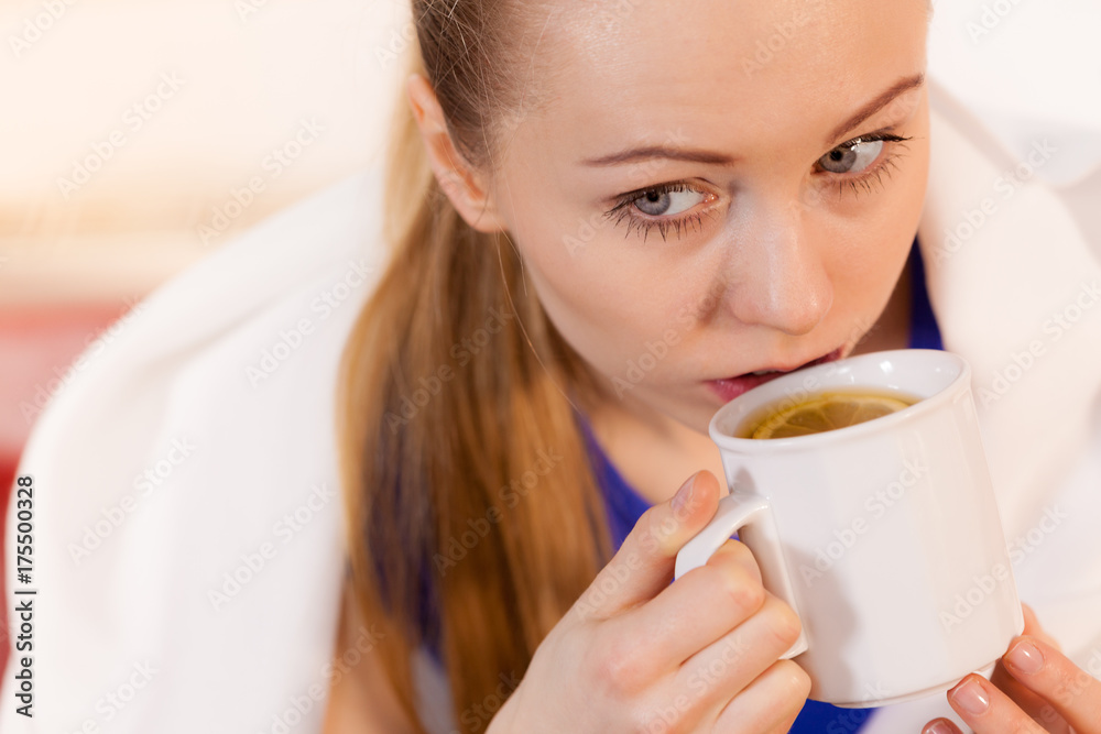 Woman lying on sofa under blanket drinking tea Woman lying on sofa under blanket drinking tea