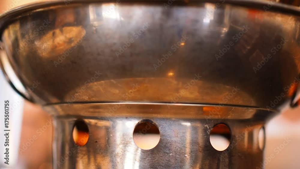 Solid alcohol heating flame lid from shiny stainless steel hot pot bowl base round hole pattern, with reflection of dining table in Thai local restaurant