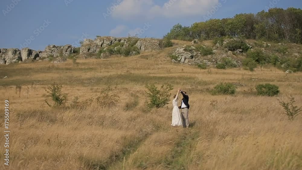 Girl and guy in the field near the cliff. Happy couple dancing against the background of rocks and blue sky. Happy couple in love in the field. Girl and guy in the field near the cliff. Happy couple dancing against the background of rocks and blue sky. Happy couple in love in the field.