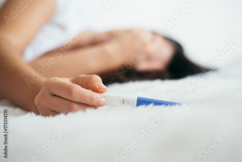 Upset woman lie sad in the bed with negative pregnancy test photo