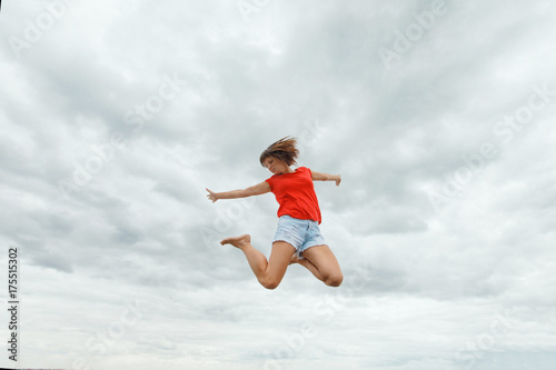 fitness, sport, victory, success and healthy lifestyle concept - happy woman winning and coming jumping in air over sky background