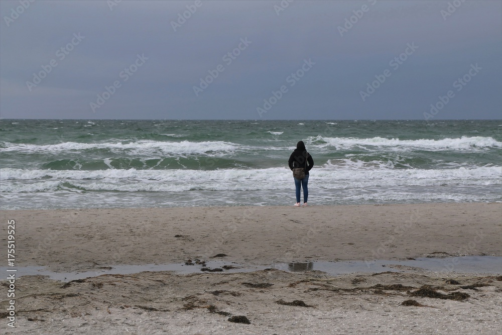 Frau steht alleine am Strand und blickt auf das Meer Frau steht alleine am Strand und blickt auf das Meer