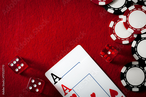 gambling and addiction to games of chance concept with a dark themed image of dice used in the casino game of craps, ace cards and splashed chips on a red felt with copy space with long shadows photo