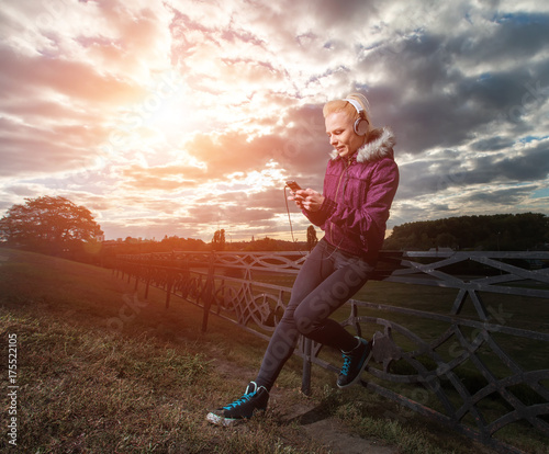 Sport girl. Young woman listening to music with headphones from her phone during exercise. Woman on the background of the sunset and blue sky.