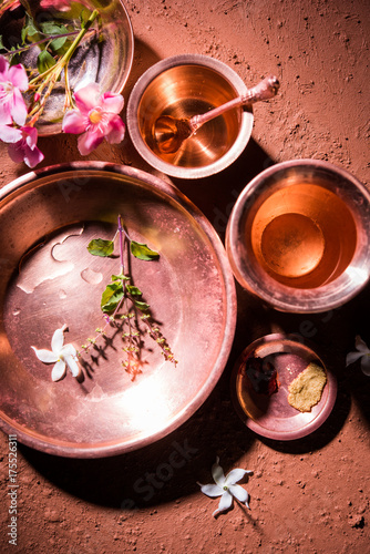 copper kalash, glass, spoon and plate used by Bramhins after sacred thread ceremony while performing Sandhya Vandanam or Sandhya Kriya, over clay background with tulsi or basil leaves & flowers

 photo