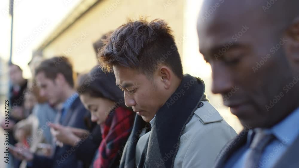 Diverse business group looking at smartphones while waiting in line Diverse business group looking at smartphones while waiting in line