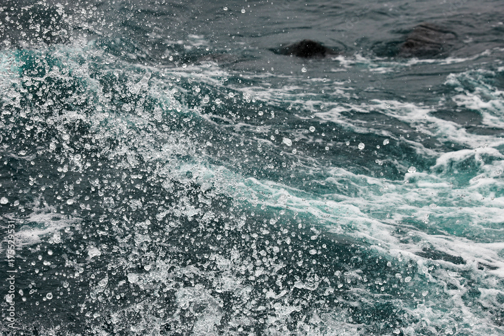 Naklejka premium Boiling surface of water under the influence of strong wind. Splashes and drops of water scatter in different directions. Cold cyan water background.