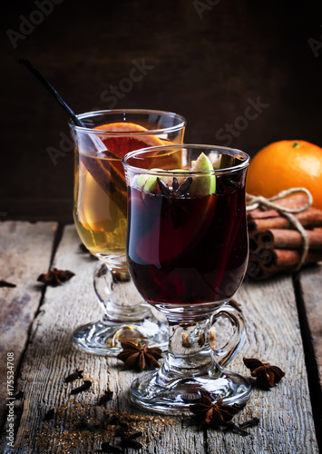 Hot mulled wine with white and red wine, spices and fruits, vintage wooden background, selective focus