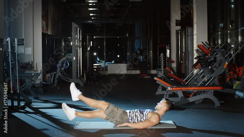 Strong sportsman working on core strength doing scissor kick and flutter kick on floor mat in cross fitness gym photo