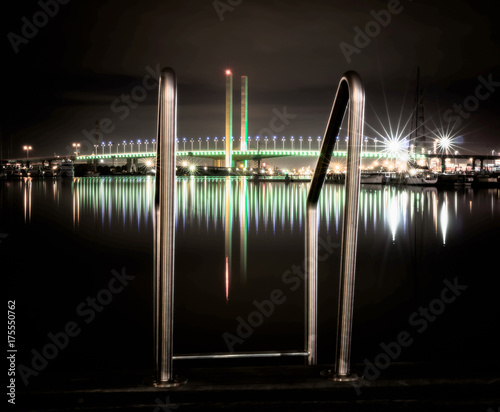 Bolte bridge at night with ladder in the foreground on a cloudless night in winter. The bolte bridge is green and reflecting in the water. photo