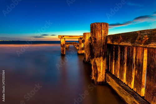 Wodden pier a dusk on a very calm day at the beach in Australia. The sky is blue and the atrmosphere is warm.