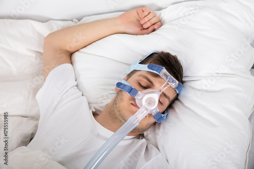 Man Lying On Bed With Sleeping Apnea And CPAP Machine