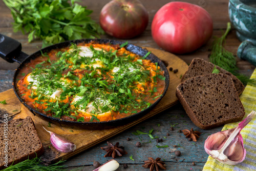 Shakshuka - jewish traditional recipe. Breakfast with fried eggs, tomato sause, pepper and green