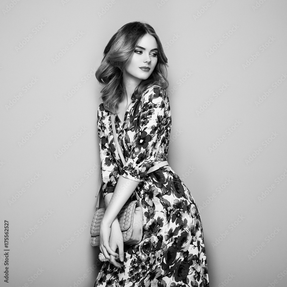 Fototapeta premium Blonde Young Woman in Floral Spring Summer Dress. Girl posing on a White Background. Stylish Wavy Hairstyle. Fashion photo. Glamour Lady with Handbag. Black and White photo